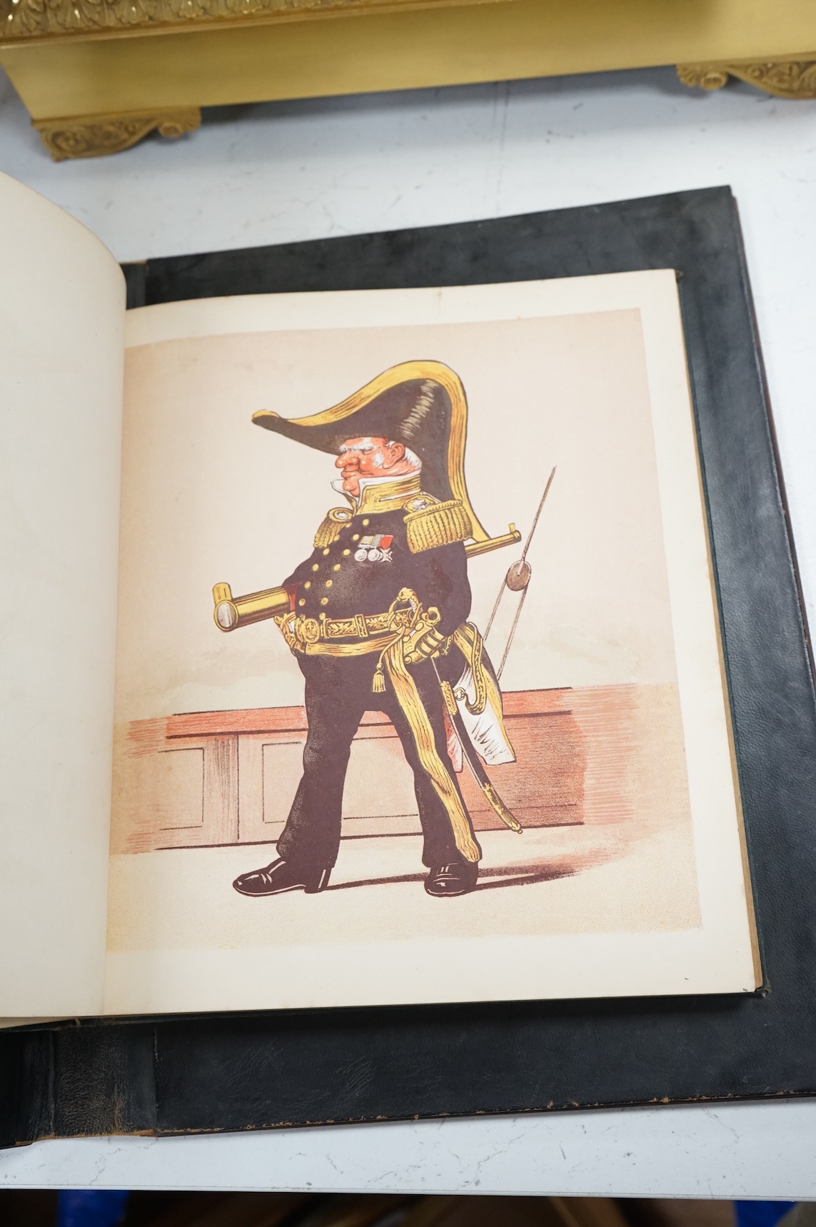 An olive and marquetry desk blotter, Duke of Wellington on horseback and his coat of arms, together with a cloth and gilt book, Army and Navy Drolleries by Captain Seccombe